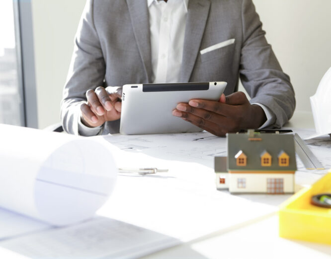 Selective focus. Design and architecture. Cropped shot of African architect holding digital tablet, developing new real estate project, sitting at desk with architectural tools and scale model house Selective focus. Design and architecture. Cropped shot of African architect holding digital tablet, developing new real estate project, sitting at desk with architectural tools and scale model house